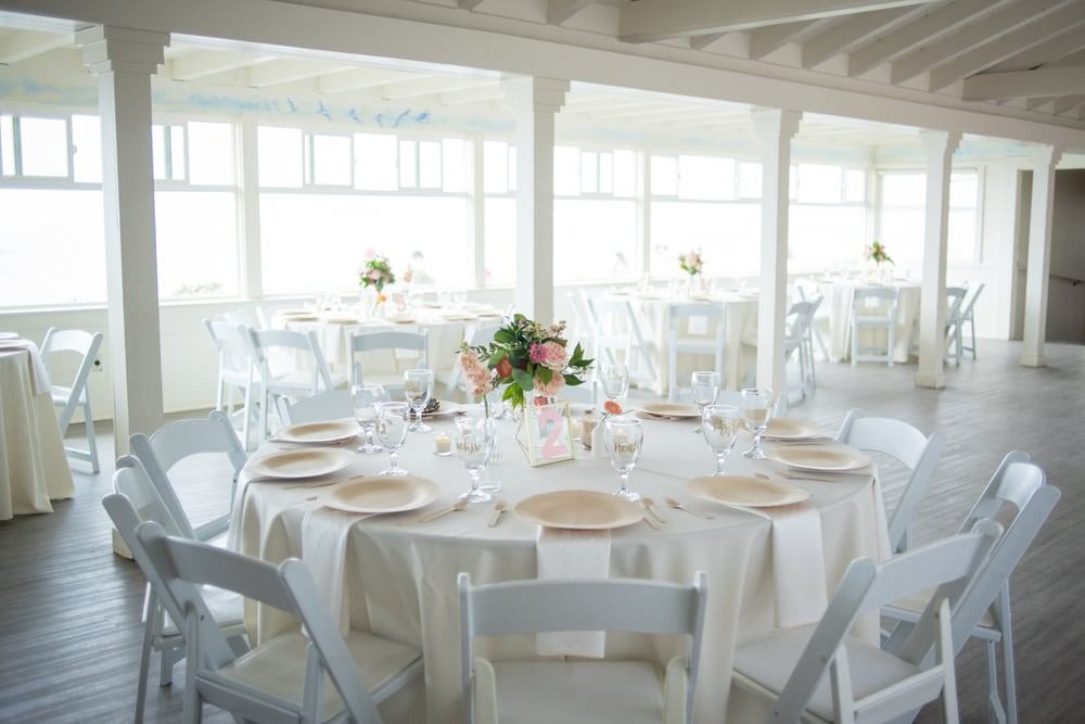 Elegant white banquet setup with floral centerpiece under natural light.