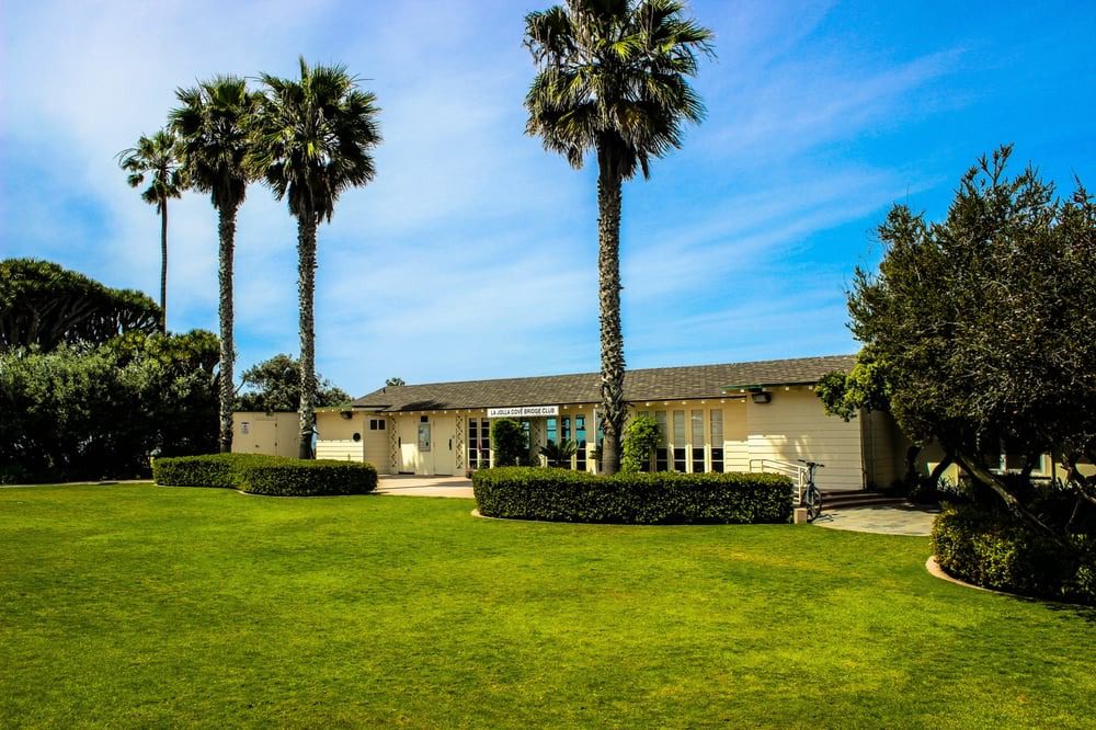 Single-story house with palm trees and green lawn under blue sky.